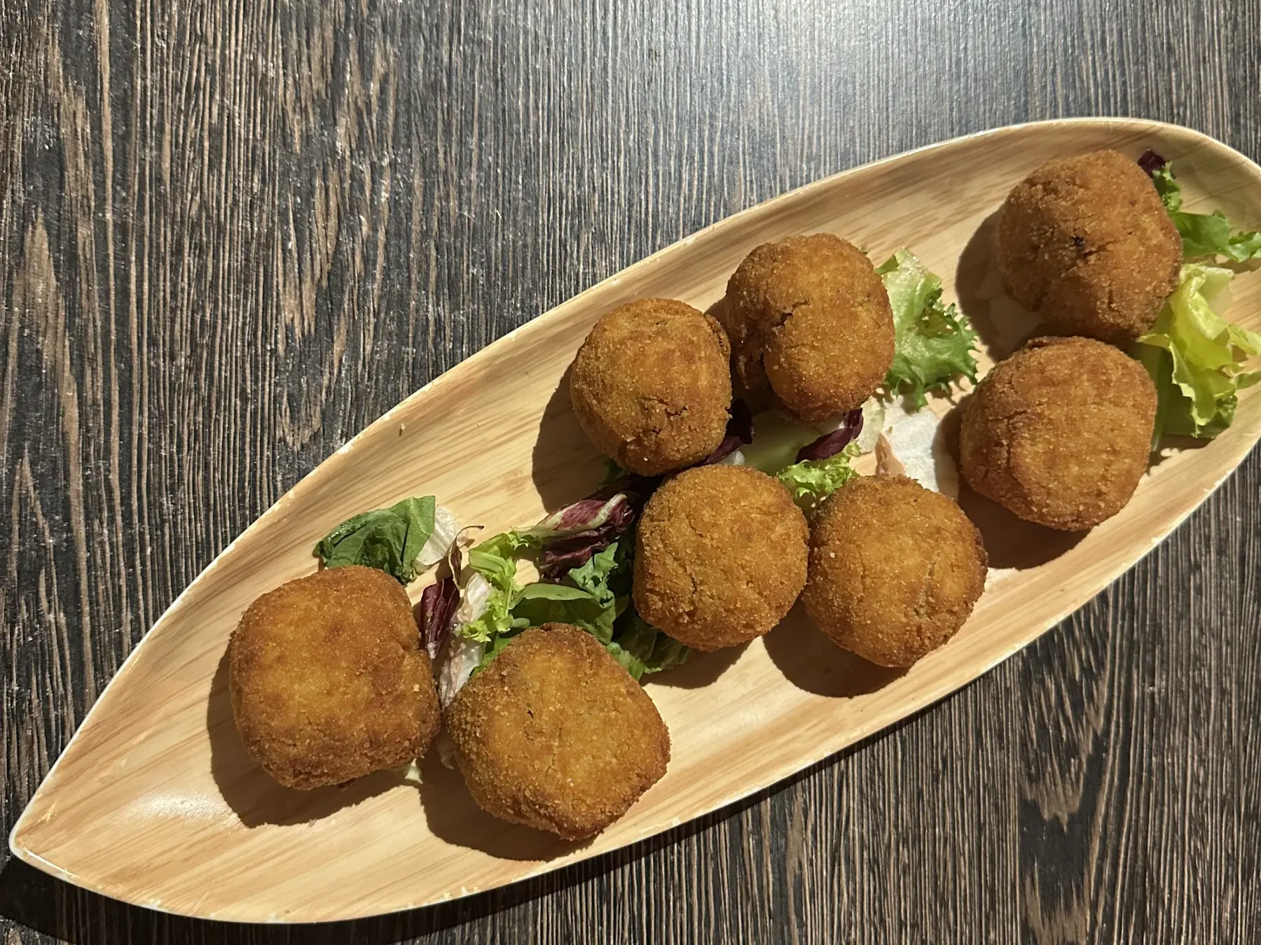 Croquetas caseras recién fritas, vistas desde arriba sobre una tabla de madera alargada