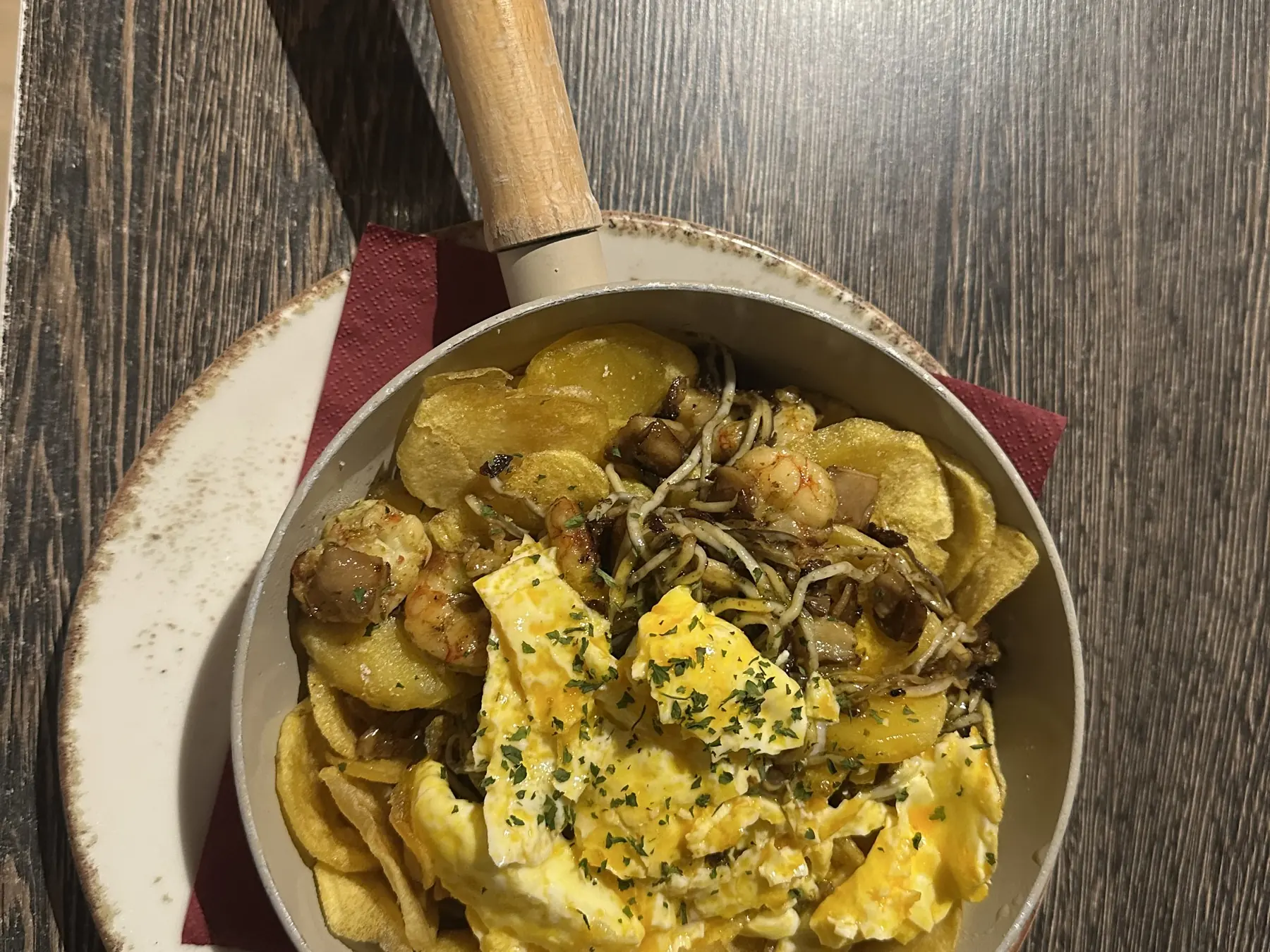 Tixola con gulas, setas y langostinos vista desde arriba: sartén de mango de madera con patatas, huevo y gulas